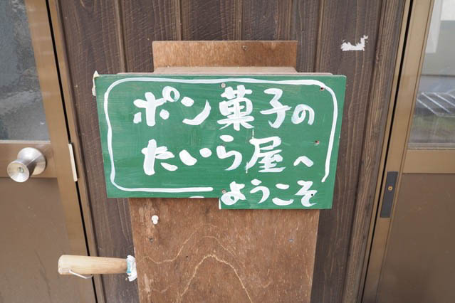 緑色の看板に白い字で「ポン菓子のたいら屋へようこそ」と書いてあります